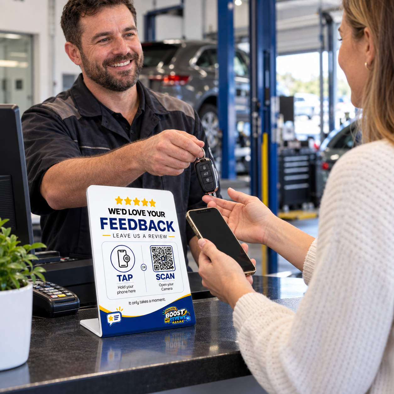 Automotive customer holding a smartphone beside a Boost My Reviews counter stand during vehicle handover.