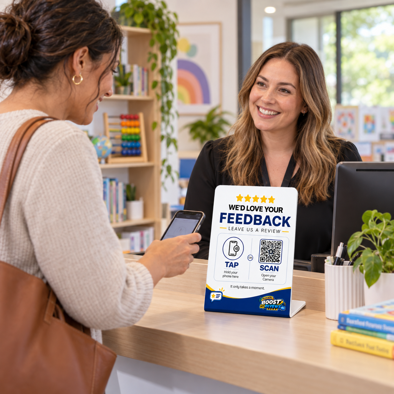 Adult learner holding a smartphone near a Boost My Reviews counter stand at an education reception desk.