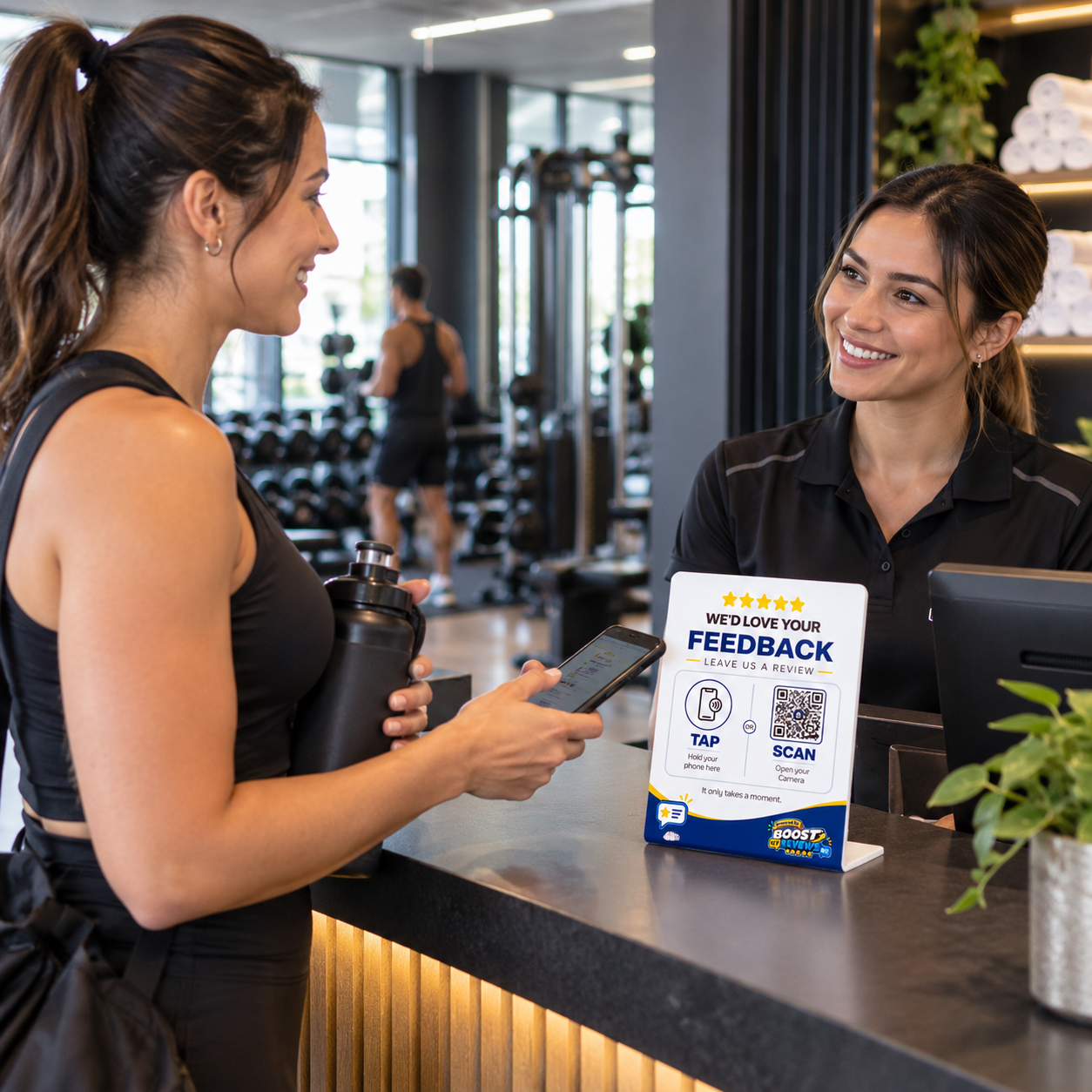 Gym member holding a smartphone beside a Boost My Reviews counter stand after a workout.