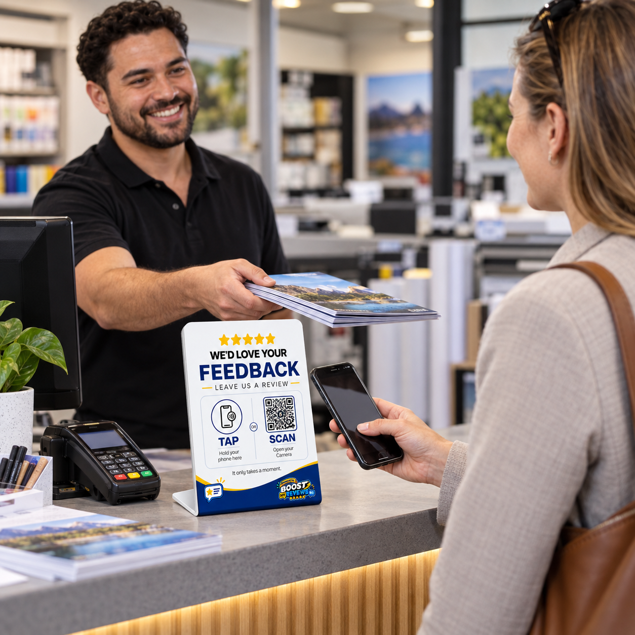 Print-shop customer preparing to use a Boost My Reviews counter stand while collecting an order.